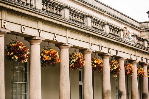 A photo of the pillars outside the Royal Pump Rooms, interspersed with orange flowers in hanging baskets.
