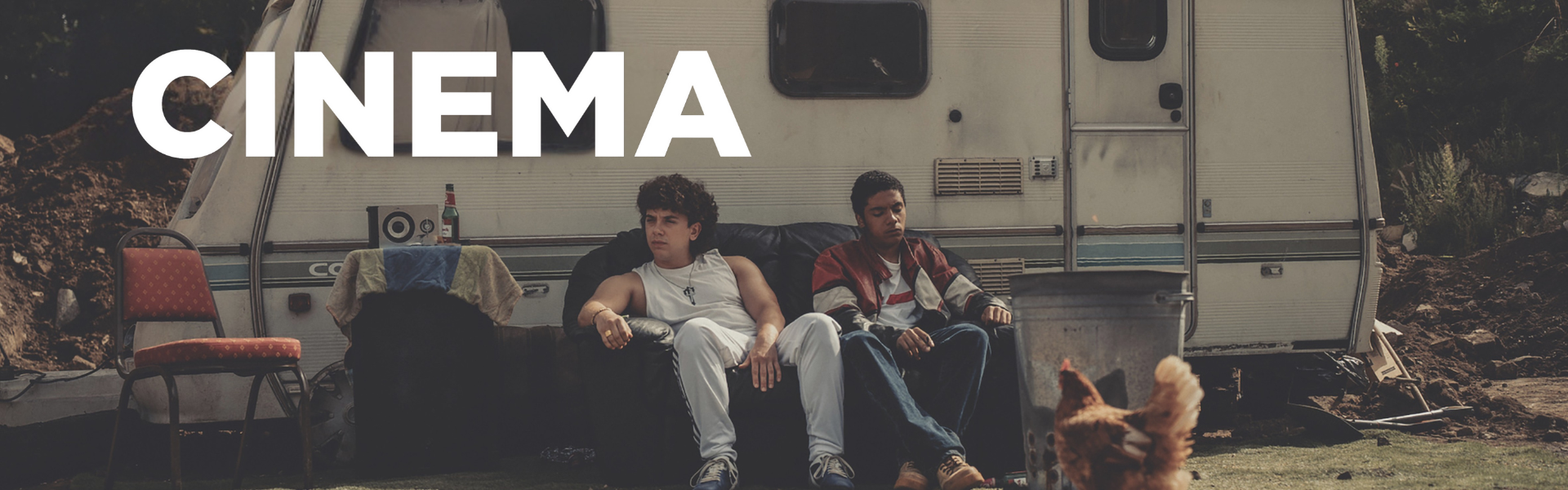 2 young males sitting on a sofa in front of a caravan.